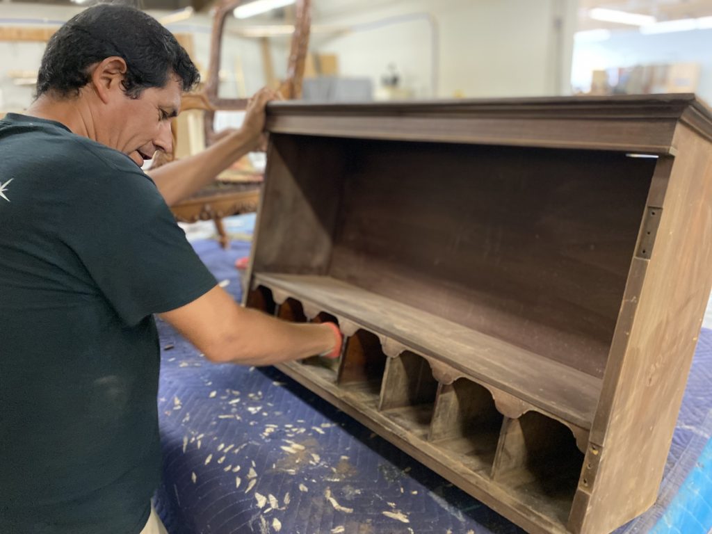 A skilled craftsman carefully sanding the mahogany surface of a mid-19th century bureau desk between coats of a new finish, ensuring a flawless restoration with attention to detail.