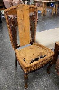 An uncovered Victorian-era chair frame with visible burlap, worn-out padding, and traces of previous modifications, revealing its antique craftsmanship.