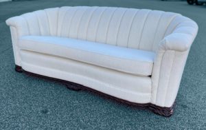 Side view of a restored art deco sofa featuring a luxurious ivory boucle upholstery and refinished wood detailing.