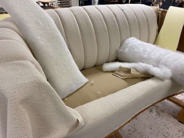 Restoration process of a vintage channel-back sofa with new ivory boucle fabric being carefully applied by Finish Pros experts.