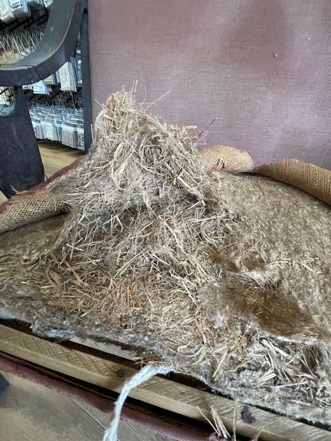 Straw and hay stuffing inside an antique chair exposed during upholstery removal at Finish Pros in Raleigh, NC