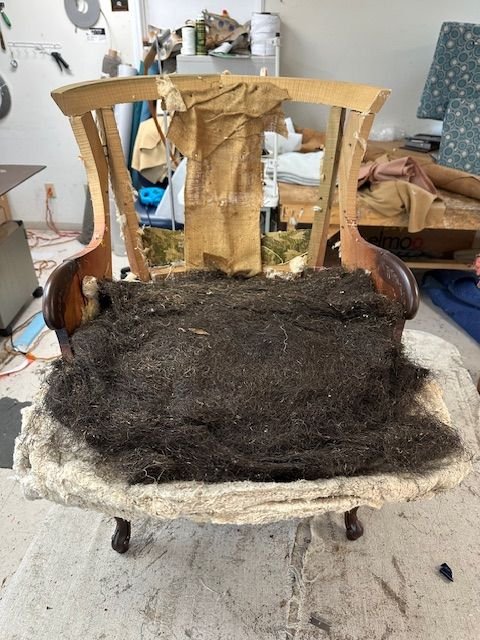 Deconstructed armchair revealing layers of old horsehair and cotton padding during restoration