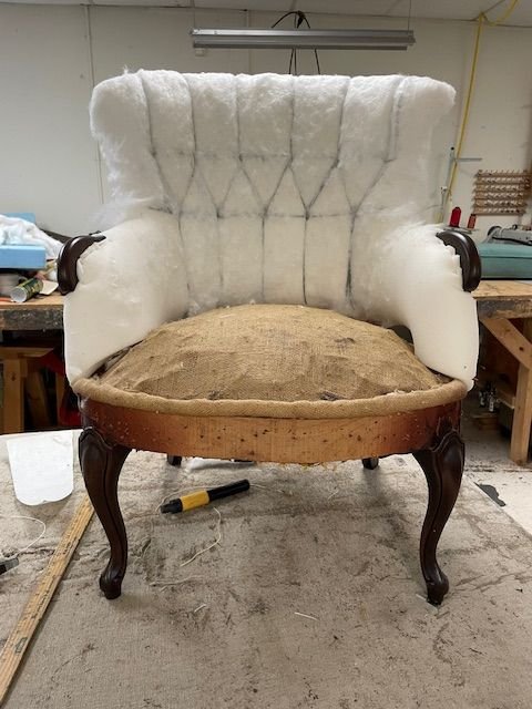 Antique tufted chair in mid-upholstery process showing cotton and foam padding layers during restoration