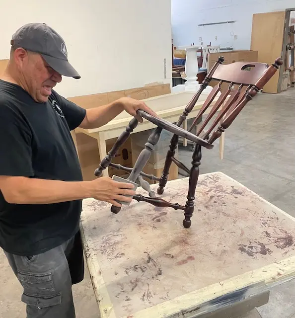 Technician at Finish Pros sanding between coats of clear lacquer finish on a restored Kling maple dining chair in the Raleigh NC workshop.