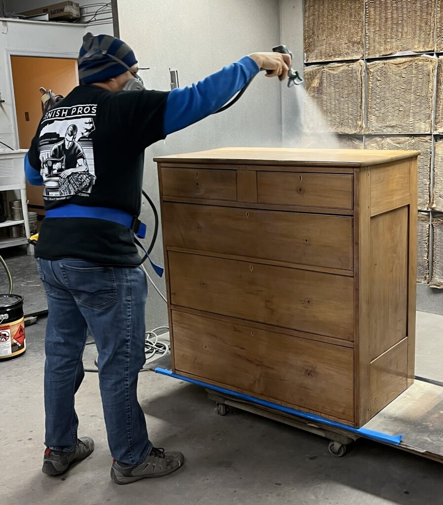 Our spray booth specialist expertly applies a natural stain to a light wood furniture piece, enhancing its grain while achieving a clean, modern finish.