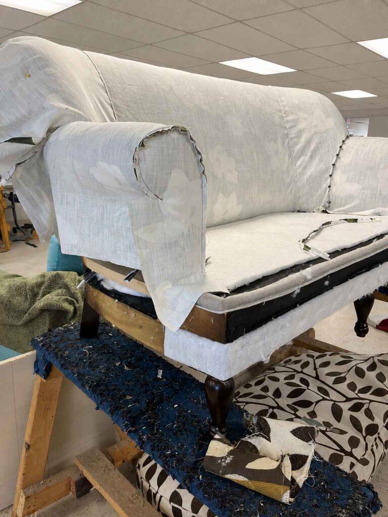 What Reupholstery Costs in Raleigh, and the 7 Things That Move the Price 3 Upholsterer pin-fitting patterned fabric from the reverse side to check pattern match before sewing, Finish Pros workshop